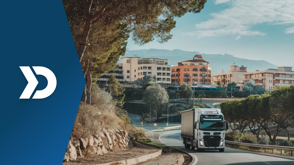 A white semi-truck driving on a curved road near a scenic urban area, symbolizing the role of mobile telematics in tracking and reducing vehicle carbon emissions.